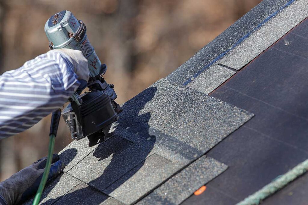 A close-up view of a house roof with clean gutters and a downspout in a leafy residential setting.