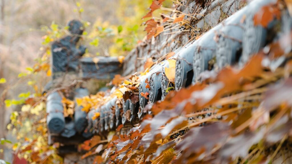 A homeowner checks a leaf-covered roof and cleared gutters beside a suburban house in autumn.